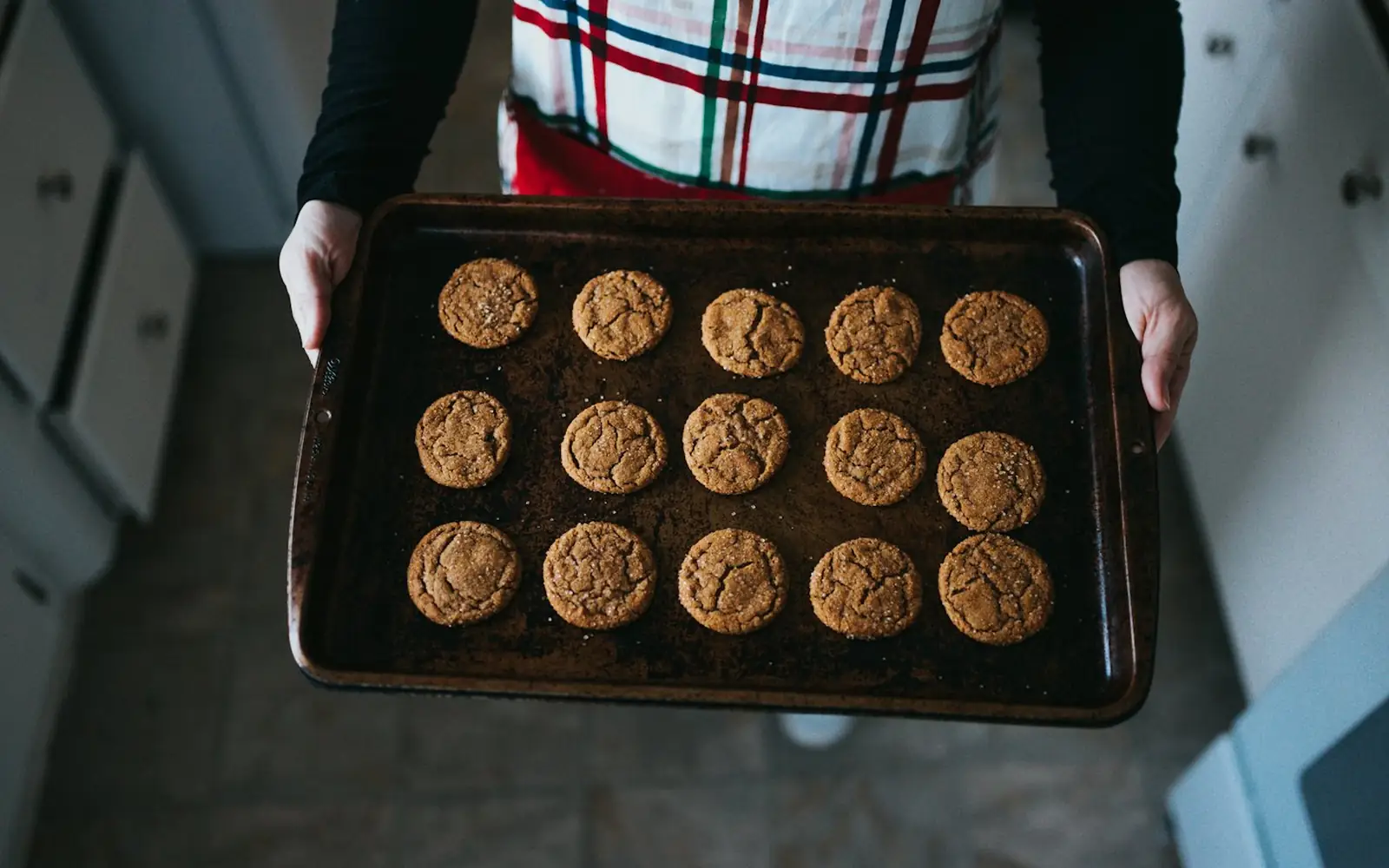 A baker holding a tray of fresh cookies